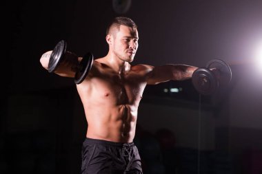 Spor salonunda spor yapan kaslı bir adam, pazularıyla egzersiz yapıyor. Güçlü erkek, çıplak karın kasları var..