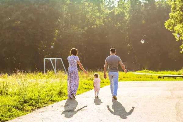 Lycklig familj utomhus aktivitet. Bakifrån av föräldrar och baby dotter ha kul och promenader i sommaren park. — Stockfoto