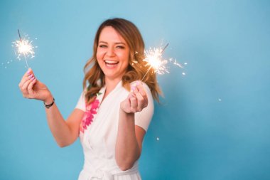 Genç mutlu kadın havai fişekleri ile kutlamak ve üzerinde mavi arka plan gül