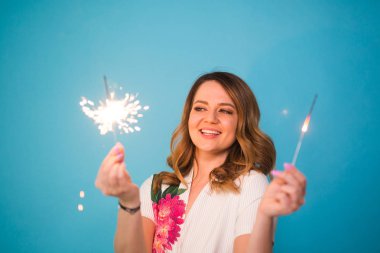 Genç mutlu kadın havai fişekleri ile kutlamak ve üzerinde mavi arka plan gül