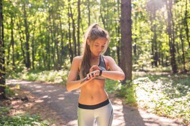 Etkinlik izleyicisi'ni veya kalp atış hızı monitörünü kullanan kadın. Açık alan fitness kavramı.