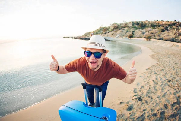 Un hombre gracioso con una maleta mostrando pulgares contra el océano azul. Concepto de viaje . — Foto de Stock