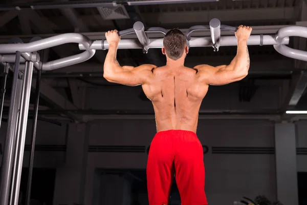Athlete muscular fitness male model pulling up on horizontal bar in a gym. — Stock Photo, Image
