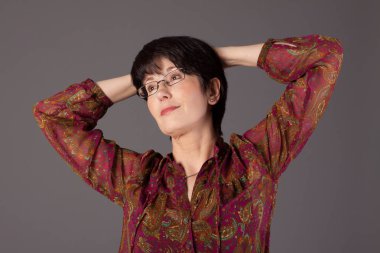 Bir gülümseyen orta yaşlı beyaz kadın gri bir arka plana dayanır portresi.