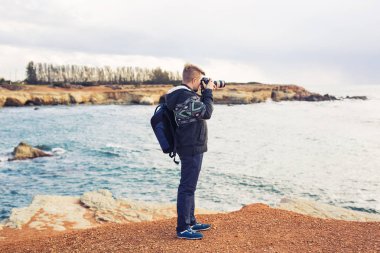 Deniz ve kayalar fotoğraflarını fotoğraf makinesi ile yapım sırt çantası ile genç fotoğrafçı. Akdeniz