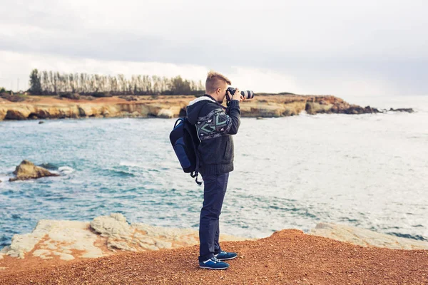 Joven fotógrafo con mochila haciendo fotos de mar y rocas con la cámara. Mar Mediterráneo — Foto de Stock