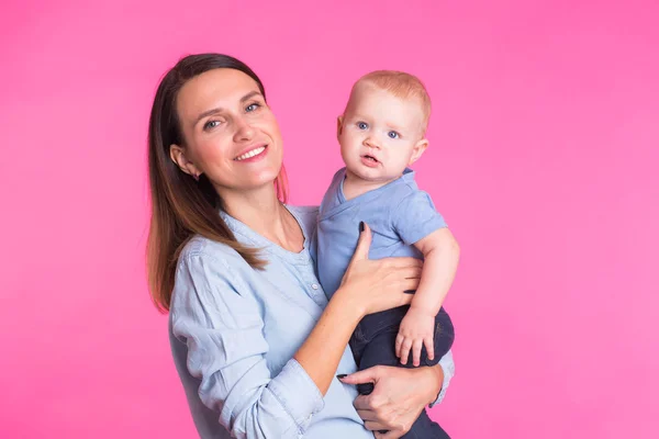 Mãe amorosa brincando com seu menino no fundo rosa — Fotografia de Stock