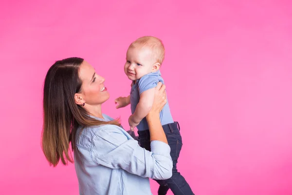 Madre cariñosa jugando con su bebé sobre fondo rosa — Foto de Stock