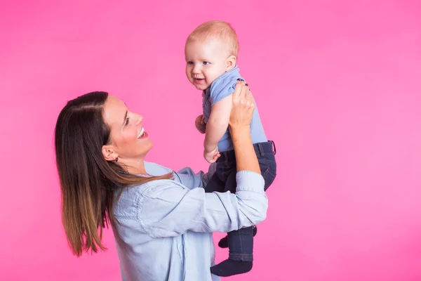 Familia, maternidad, crianza, personas y concepto de cuidado infantil - madre feliz sostiene adorable bebé sobre fondo rosa — Foto de Stock