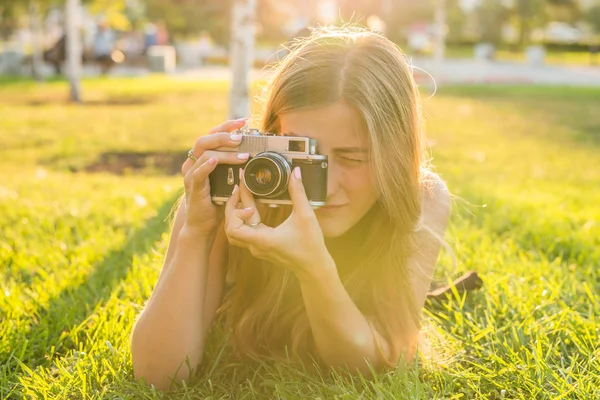 Glimlachend jonge vrouw met behulp van een retro camera om foto te nemen in het park. — Stockfoto
