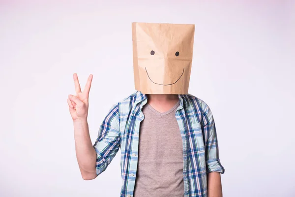 Hombre desconocido mostrando signo de victoria con una bolsa de papel en la cabeza sobre fondo blanco — Foto de Stock