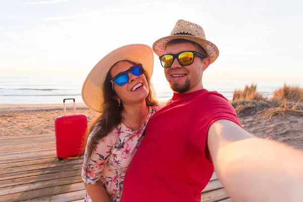 Feliz casal viajante apaixonado tirar uma selfie no telefone com malas na praia em um dia ensolarado de verão — Fotografia de Stock