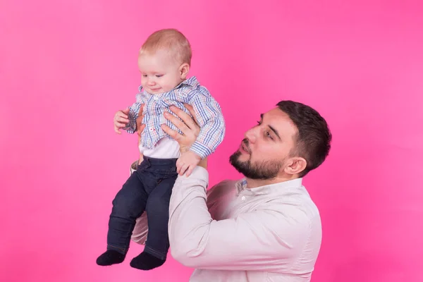 Padre feliz con un hijo pequeño aislado sobre un fondo rosa — Foto de Stock