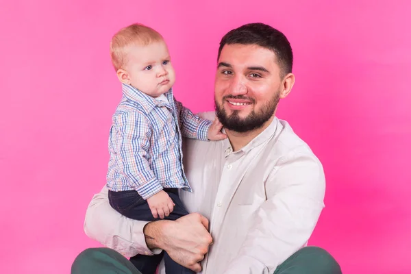 Padre feliz con un hijo pequeño aislado sobre un fondo rosa — Foto de Stock