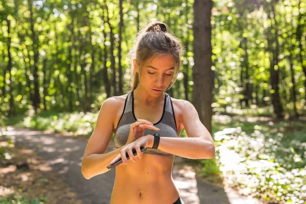 Активна дівчина використовує фітнес-трекер розумний годинник біжить на літній природі на відкритому повітрі, дивлячись на дані про здоров'я під час спортивної діяльності — стокове фото
