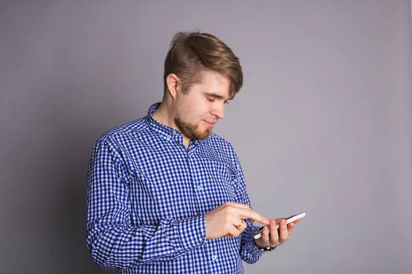 Joven escribiendo un mensaje de texto en su celular sobre un fondo gris — Foto de Stock