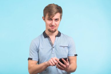 Genç adam cep telefonunu mavi bir arka plan üzerinde metin mesajı yazmaya