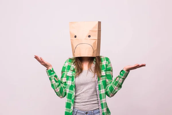 Chica infeliz con emoticono triste en bolsa de papel en la cabeza sobre fondo blanco — Foto de Stock