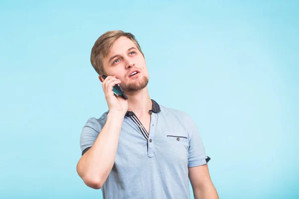 Портрет молодого человека, разговаривающего по телефону на синем фоне — стоковое фото