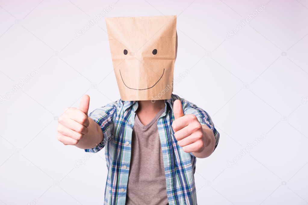 Unknown man showing thumbs up with a paper bag on his head on white background