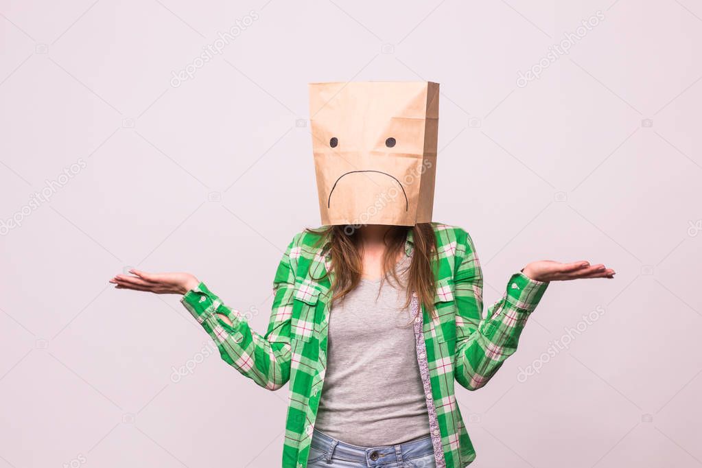 Unhappy woman with sad emoticon in front of paper bag on her head on white background