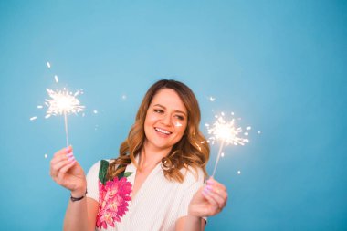Genç mutlu kadın havai fişekleri ile kutlamak ve üzerinde mavi arka plan gül