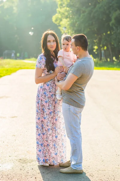 Feliz carrera mixta familia actividad al aire libre. Los padres y la hija del bebé se divierten y caminan en el parque de verano . — Foto de Stock