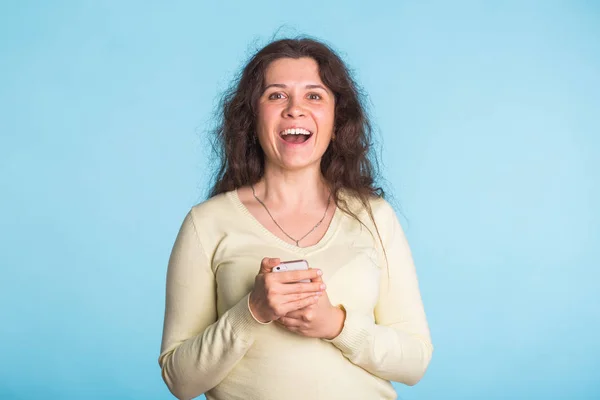 Mujer sonriente joven usando el teléfono móvil contra fondo azul —  Fotos de Stock
