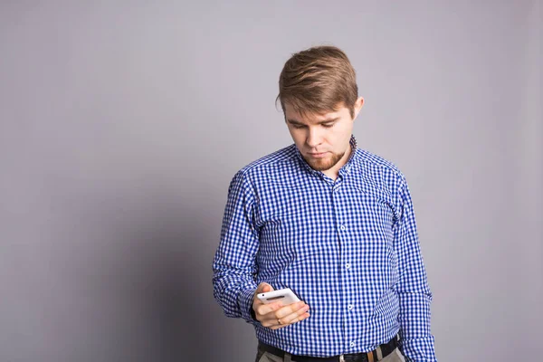 Молодой человек печатает смс на мобильном на сером фоне — стоковое фото