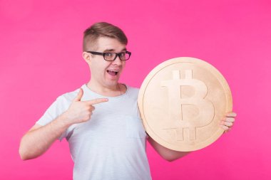 Mutlu genç adam, pembe arka plan büyük altın bitcoin tutarak. Kripto para birimi, sanal para, internet ve ekonomi kavramı
