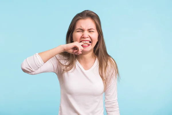 Mujer mordiendo el dedo con los dientes, expresa dolor e ira sobre fondo azul — Foto de Stock