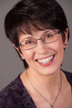 Bir gülümseyen zarif orta yaşlı beyaz kadın gri bir arka plana dayanır portresi.