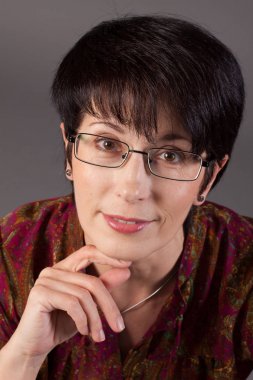 Bir gülümseyen zarif orta yaşlı beyaz kadın gri bir arka plana dayanır portresi.