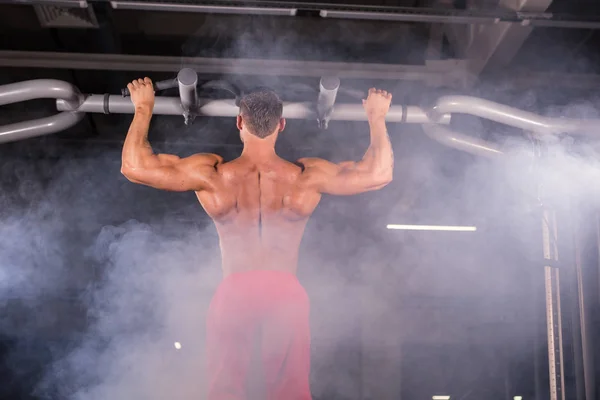 Athlete muscular fitness male model pulling up on horizontal bar in a gym.