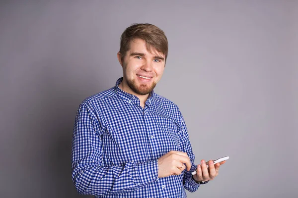 Νεαρός άνδρας μήνυμα αποστολή γραπτών μηνυμάτων στο smart phone που απομονώνονται σε γκρι φόντο. Χαμογελαστός ο τύπος κρατώντας το smartphone και το κοιτάς. — Φωτογραφία Αρχείου
