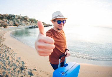 Komik adam çanta gösterilen mavi okyanusun karşı başparmak. Seyahat kavramı.