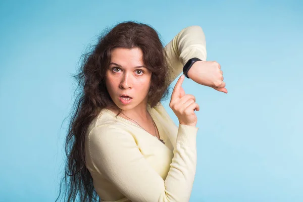 Aufgeregte junge Frau zeigt mit ihrer Armbanduhr auf blauen Hintergrund — Stockfoto