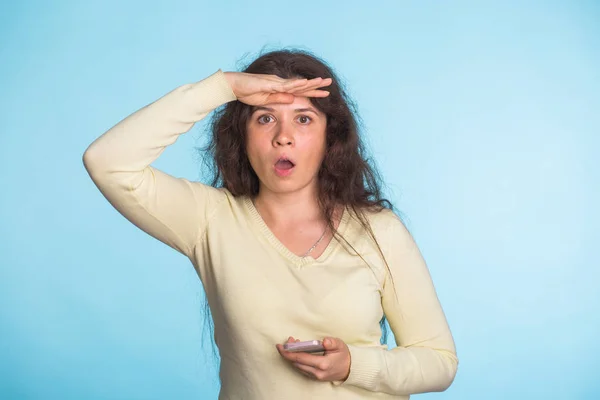 Jovem mulher animada segurando telefone celular e olhando para a frente sobre fundo azul — Fotografia de Stock