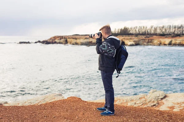 Joven fotógrafo con mochila haciendo fotos de mar y rocas con la cámara. Mar Mediterráneo — Foto de Stock