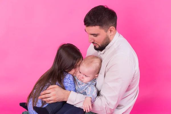 Padre guapo llevando a su pequeña hija e hijo bebé sobre fondo rosa — Foto de Stock