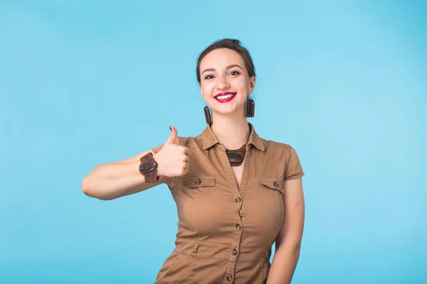 Alegre joven morena caucásica estudiante chica mostrando los pulgares hacia arriba sobre fondo azul con espacio de copia — Foto de Stock