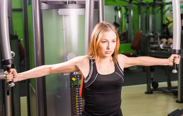 Atletische jonge vrouw werkt op simulator in gym klasse — Stockfoto