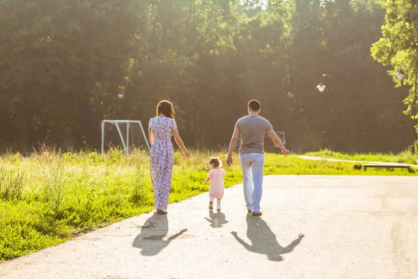 Feliz actividad familiar al aire libre. Vista trasera de los padres y la hija del bebé divirtiéndose y caminando en el parque de verano . — Foto de Stock