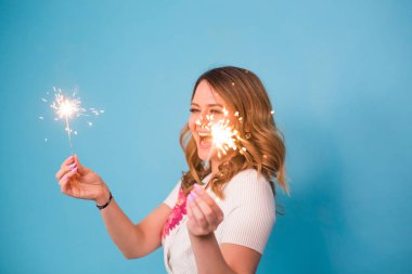 Genç mutlu kadın havai fişekleri ile kutlamak ve üzerinde mavi arka plan gül