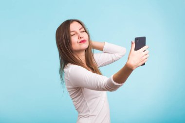 Neşeli genç kadın selfie akıllı telefonunu mavi arka plan yapma