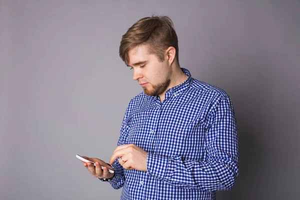 Joven escribiendo un mensaje de texto en su celular sobre un fondo gris — Foto de Stock