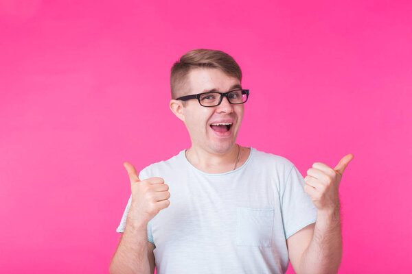 Young optimistic man on pink background showing thumbs up with positive emotions of content and happiness. Concept of satisfaction with quality and recommendation