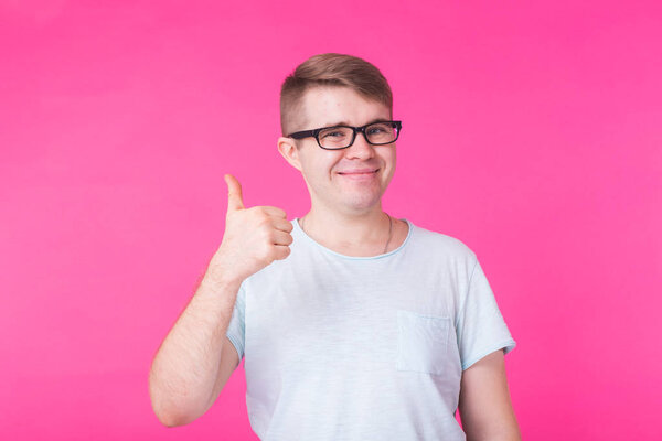 Young optimistic man on pink background showing thumbs up with positive emotions of content and happiness. Concept of satisfaction with quality and recommendation