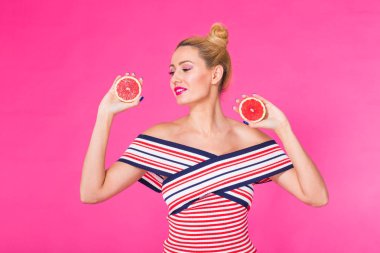 Greyfurt ile gülümseyen kız elinde pembe bir arka plan üzerinde yarım meyve kesme