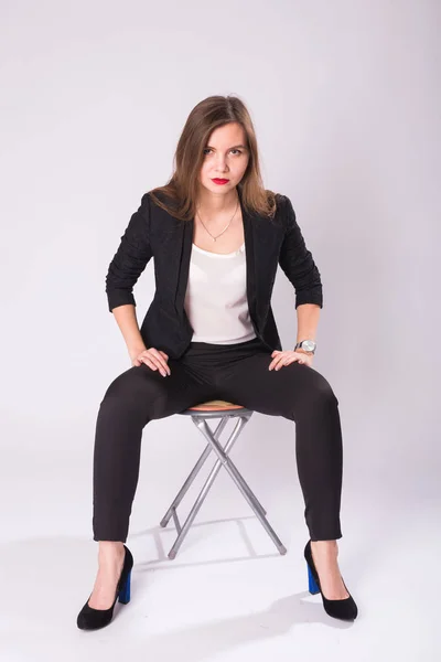 Hermosa joven mujer de negocios en traje negro se sienta en una silla sobre fondo blanco — Foto de Stock